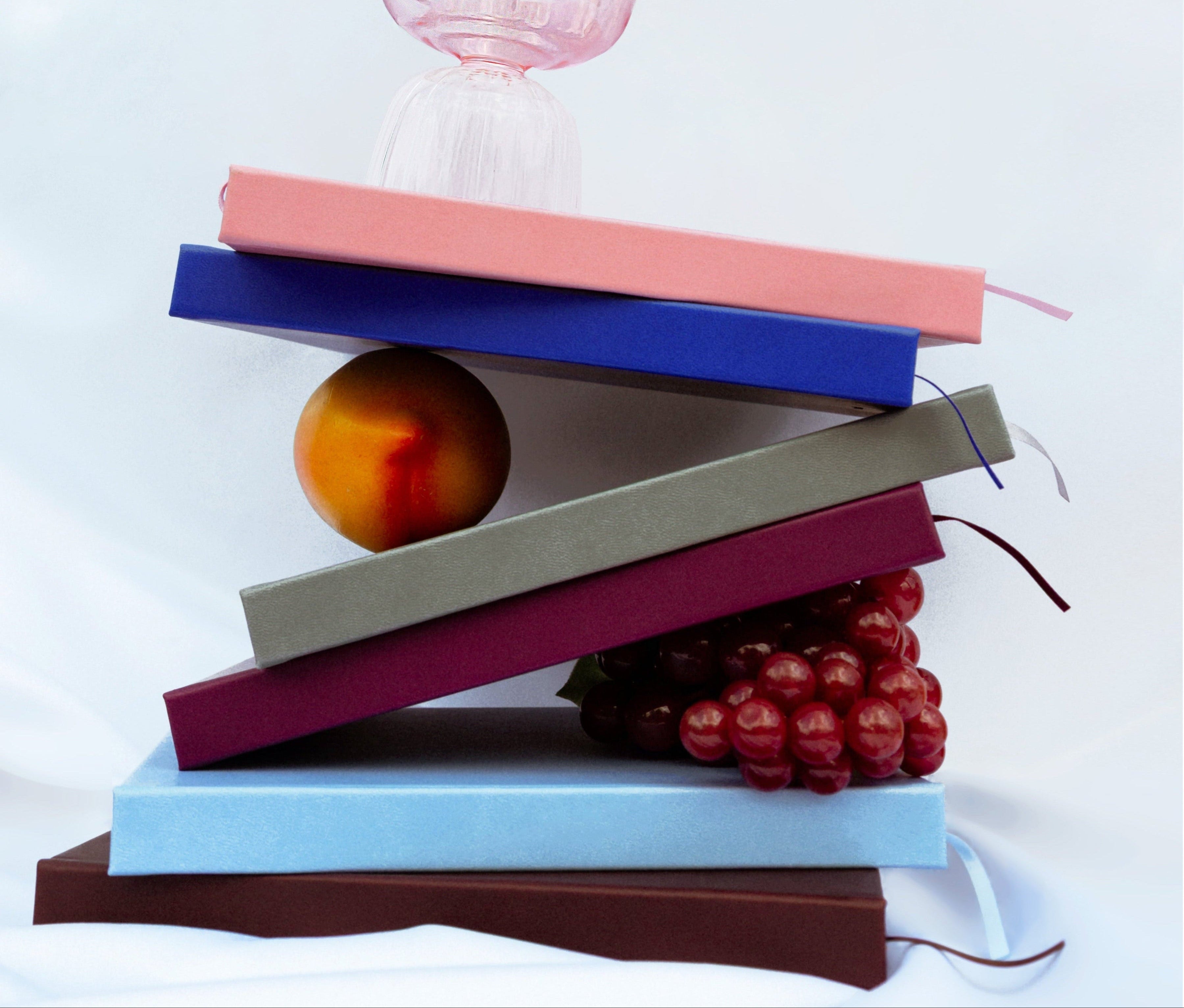 Stack of books with a glass bowl, fruit, and jewelry on a white background